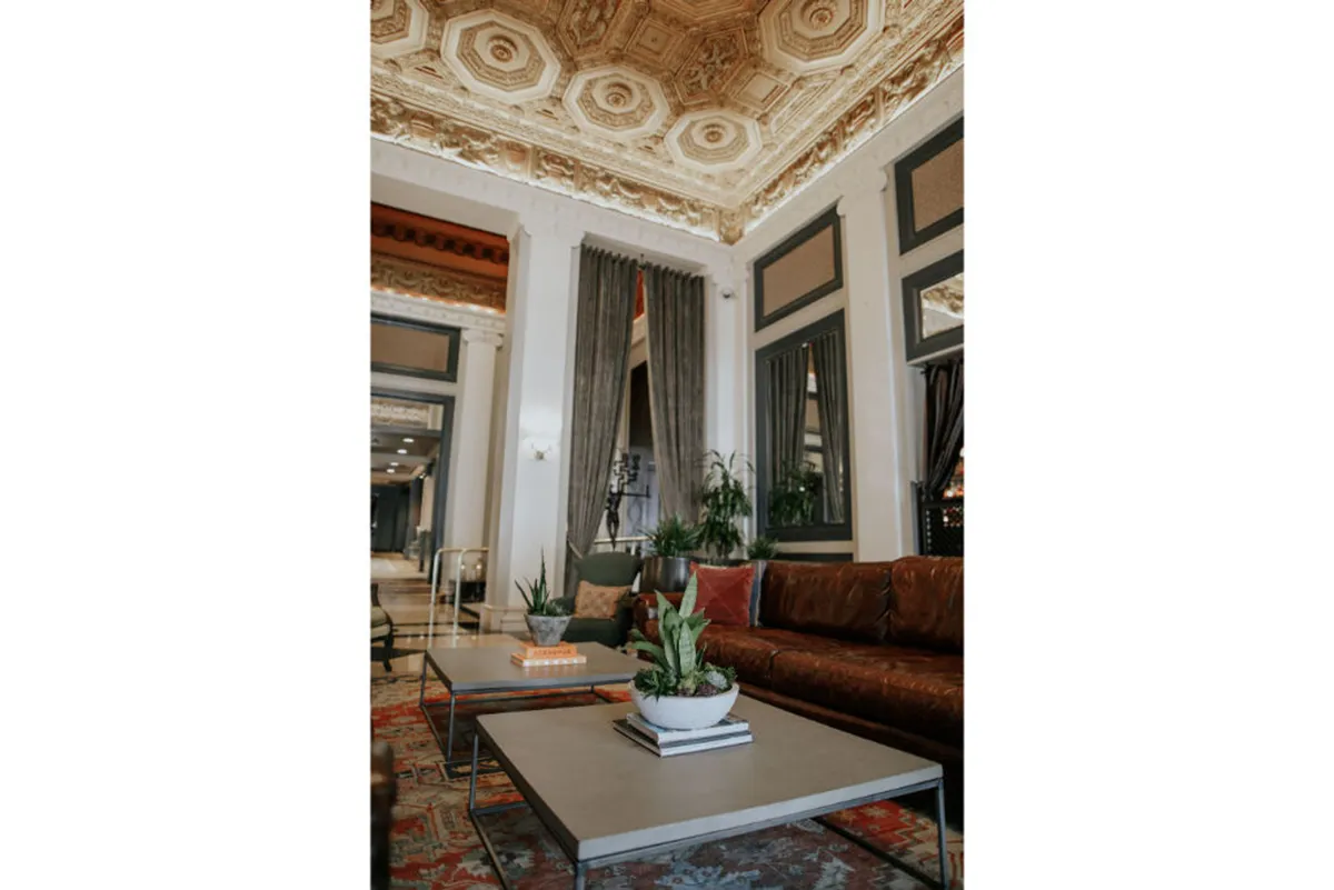 A cozy lounge area with a leather sofa, coffee tables decorated with plants, and elegant curtains, all under an ornate ceiling. The space feels welcoming and relaxed, ideal for unwinding after a day exploring the city.