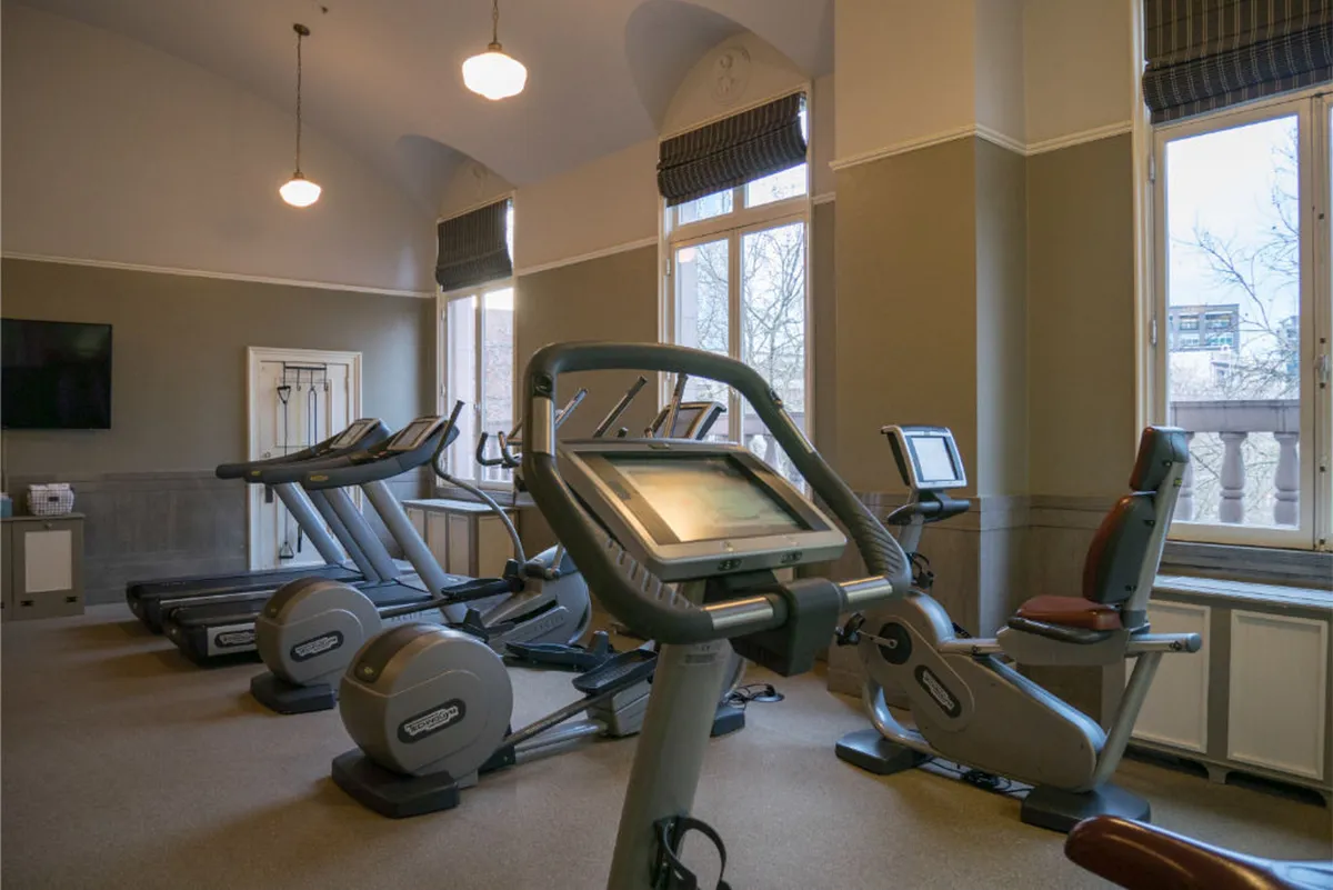 A modern fitness center with large windows, treadmills, and ellipticals. The room is bright and energizing, encouraging both individual cardio workouts and group fitness classes while offering pleasant city views.