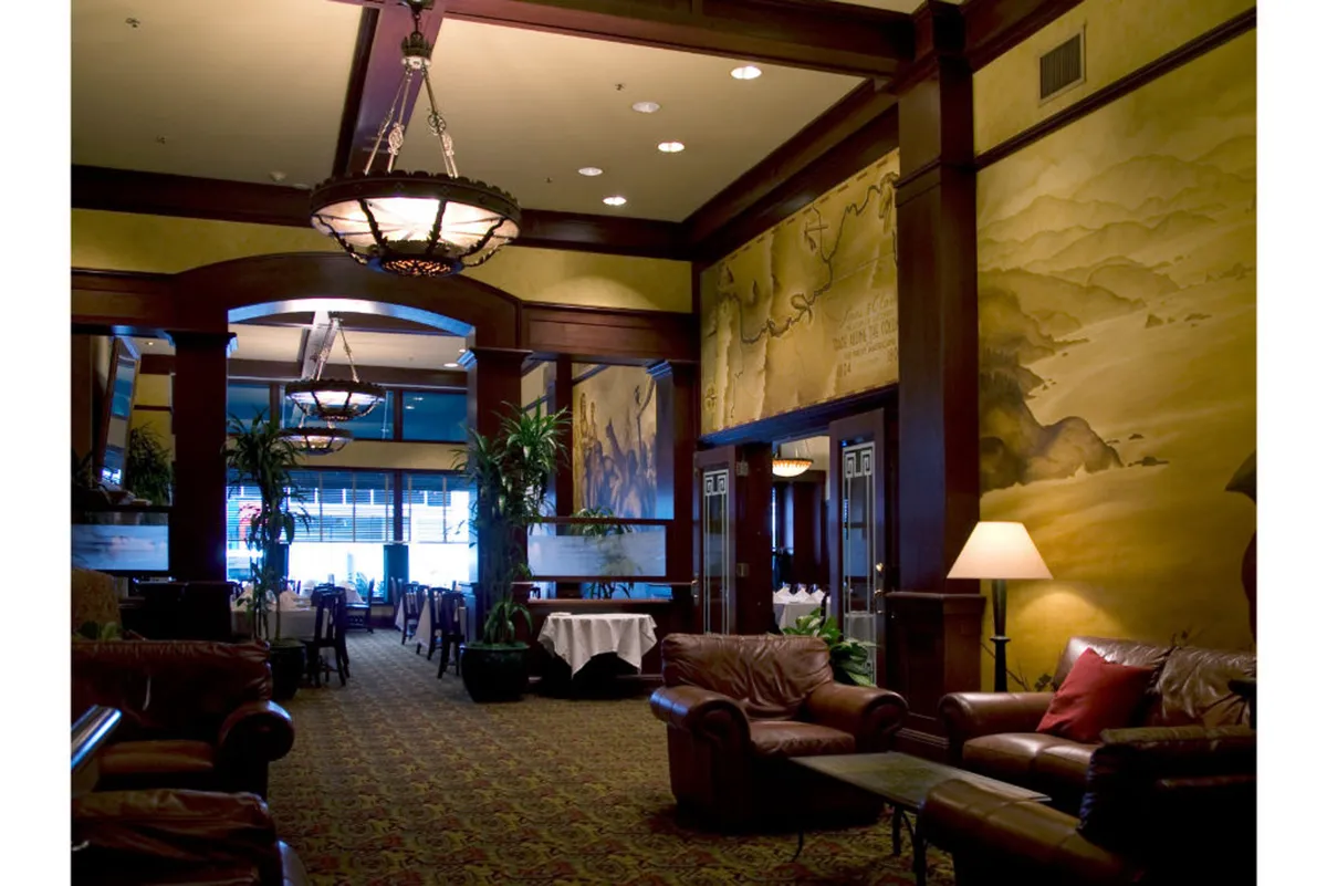 An elegant lounge area featuring leather sofas, chandeliers, decorative wall murals, and lush potted plants. The setting is sophisticated yet cozy, ideal for executive guests seeking a tranquil space to work, network, or recharge between activities.