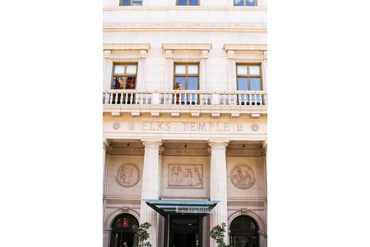 A stately exterior shot featuring the Elks Temple signage, ornate columns, and decorative sculptures. The architectural details suggest a locale rich in history and culture, ideal for exploring events, gatherings, and the artistic pulse of the neighborhood.