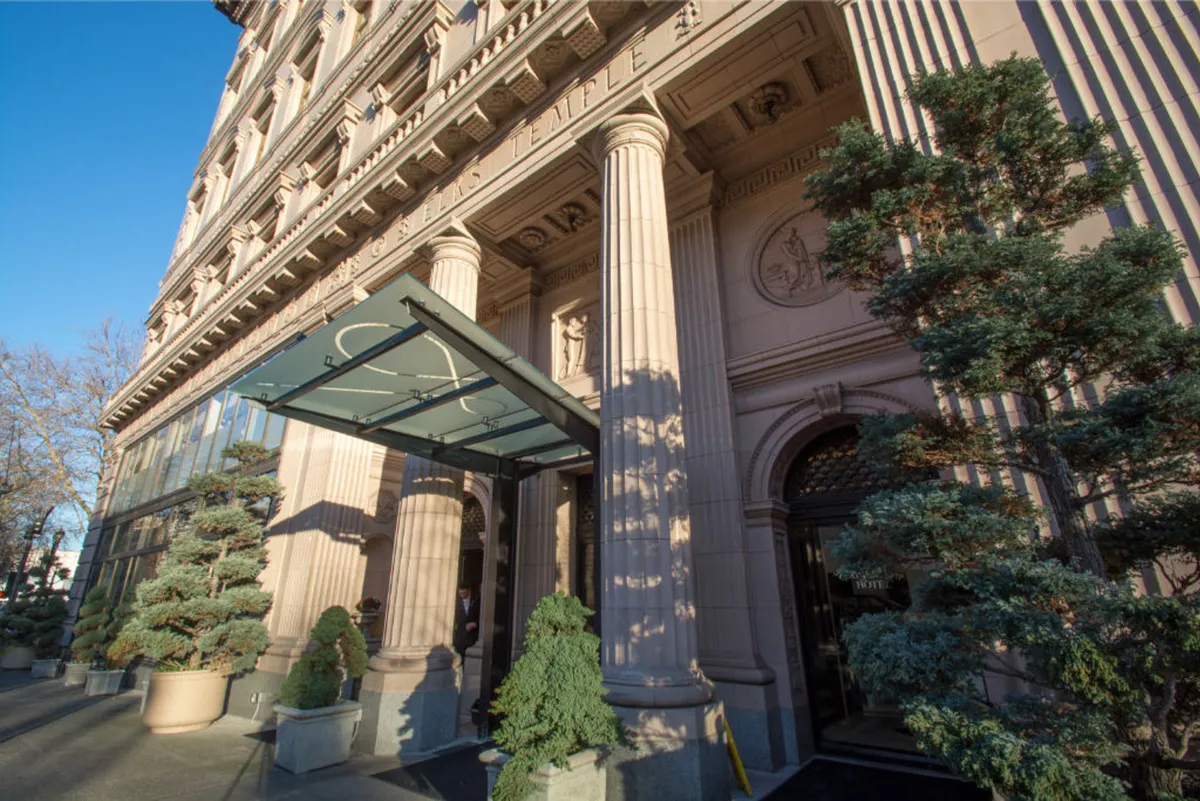 This image captures the elegant exterior of a building featuring ornate columns, a glass awning, and well-manicured shrubs. The entrance exudes a sense of luxury and sophistication, creating an inviting first impression for arriving guests.