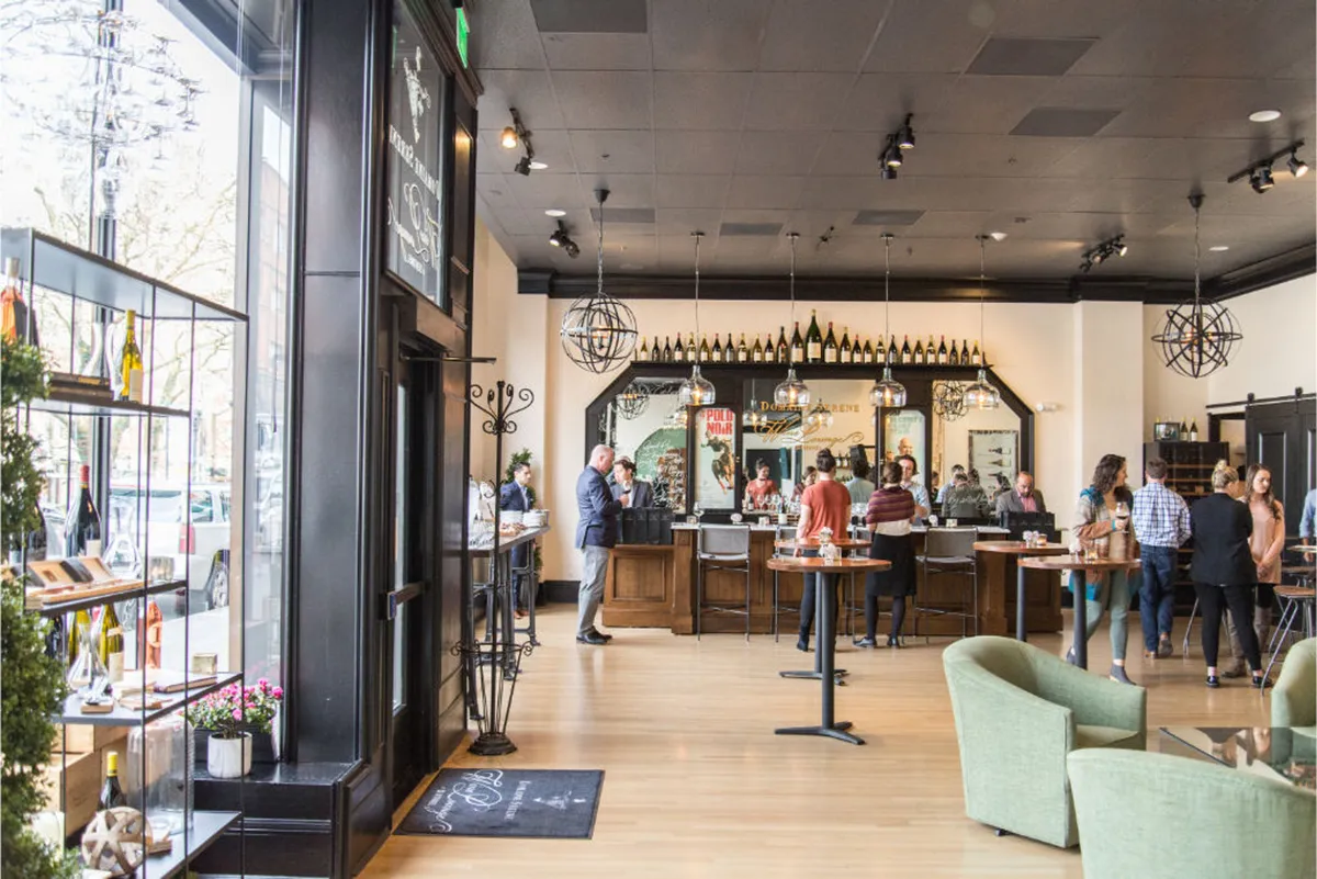 A stylish bar area featuring a sleek counter lined with wine bottles, comfortable seating, and a vibrant, social ambiance. Perfect for relaxing and enjoying a glass of wine during the daily wine hour.